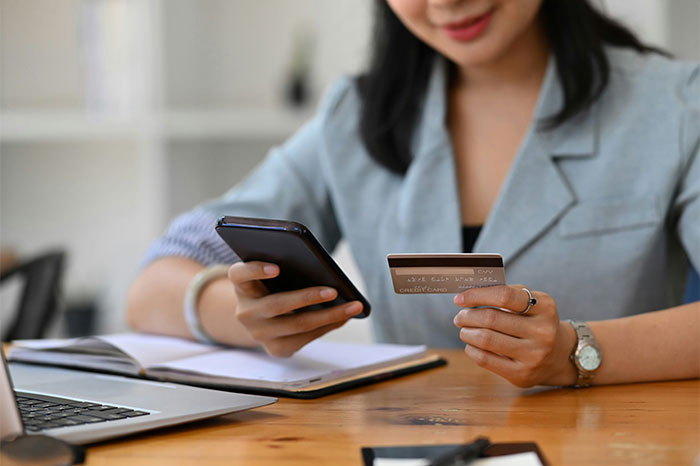 A person in a gray jacket holding a phone and credit card at a desk, contemplating No-Buy 2025 decisions. A person in a gray jacket holding a phone and credit card at a desk, contemplating No-Buy 2025 decisions.