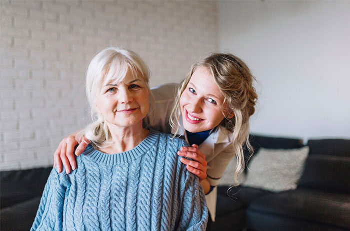 Woman smiling next to seated elderly woman, highlighting family bonds after a relationship conflict. Woman smiling next to seated elderly woman, highlighting family bonds after a relationship conflict.