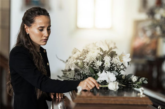Woman at a funeral, contemplating a casket with flowers, reflecting on relationship and loss. Woman at a funeral, contemplating a casket with flowers, reflecting on relationship and loss.
