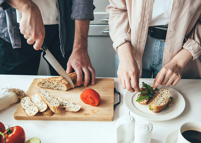 Two people preparing vegetarian sandwiches, slicing bread and adding greens, related to wedding meal discussions. Two people preparing vegetarian sandwiches, slicing bread and adding greens, related to wedding meal discussions.