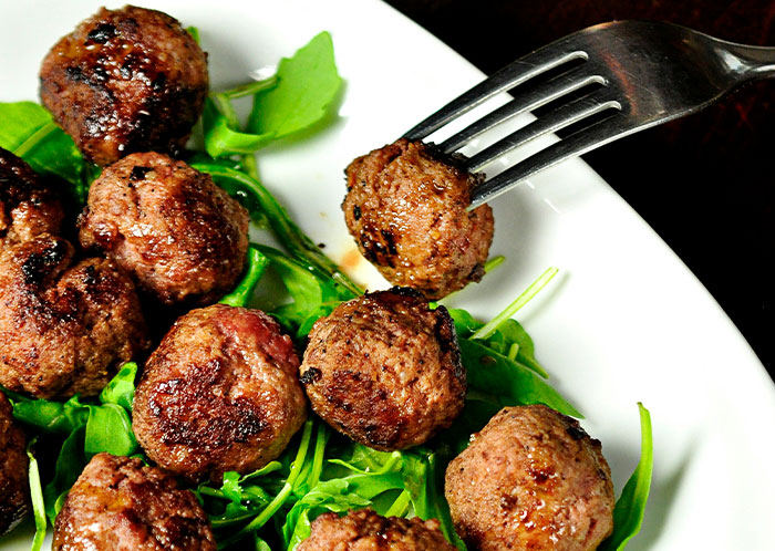 Vegetarian meatballs served on a bed of greens with a fork picking up one meatball. Vegetarian meatballs served on a bed of greens with a fork picking up one meatball.