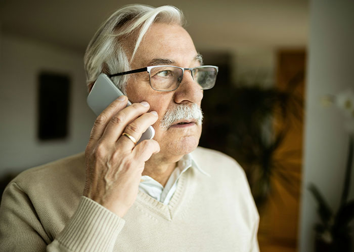 Elderly man with glasses on phone, appearing upset, in a beige sweater. Elderly man with glasses on phone, appearing upset, in a beige sweater.