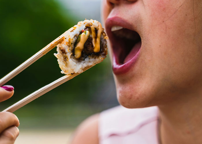 Person eating sushi with chopsticks, highlighting vegetarian meal experience. Person eating sushi with chopsticks, highlighting vegetarian meal experience.