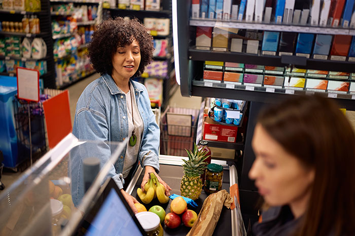 Woman at a grocery checkout doing a good deed, smiling while placing fruits on the counter. Woman at a grocery checkout doing a good deed, smiling while placing fruits on the counter.
