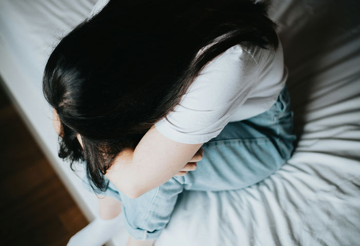 A new mom sits on a bed, hugging her knees, in a moment of distress. A new mom sits on a bed, hugging her knees, in a moment of distress.