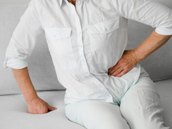 Person in white shirt and pants sitting on a couch, holding side in unexplainable pain.