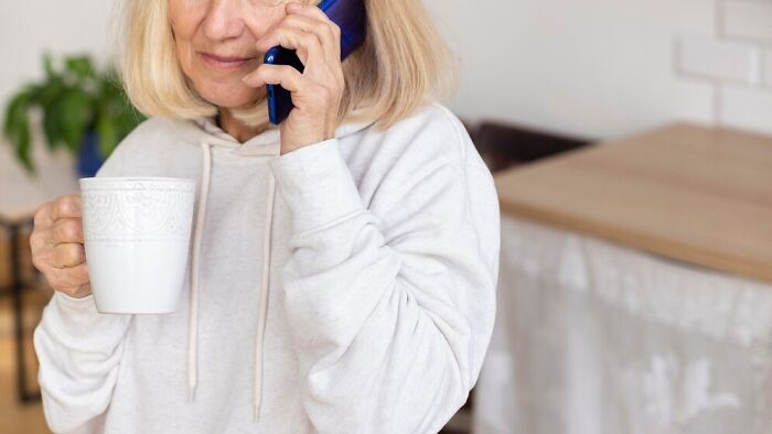 Woman talking on the phone, holding a mug, casually dressed in a light hoodie at home. Woman talking on the phone, holding a mug, casually dressed in a light hoodie at home.