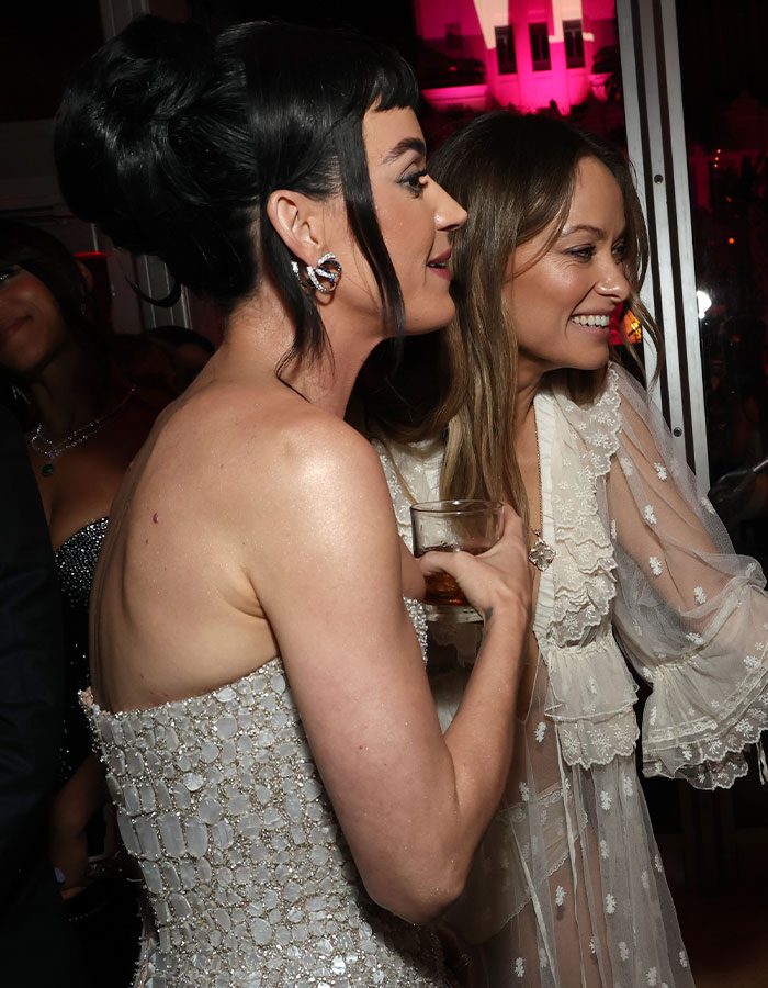 Two women in formal dresses, smiling at an event, with a drink in hand. Two women in formal dresses, smiling at an event, with a drink in hand.