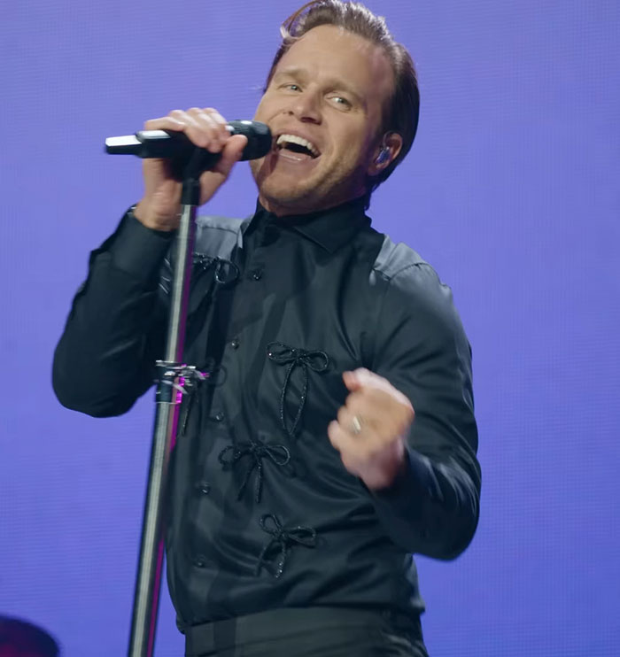 Singer performing on stage with microphone, showcasing physique transformation sparking debate between men and women. Singer performing on stage with microphone, showcasing physique transformation sparking debate between men and women.