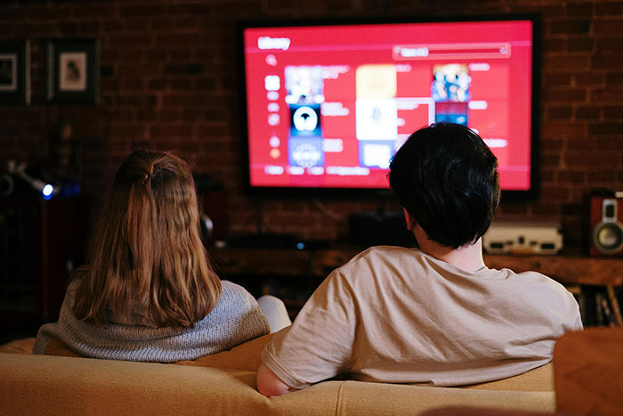 Couple watching TV on a couch, highlighting challenges of long-distance relationships and communication. Couple watching TV on a couch, highlighting challenges of long-distance relationships and communication.
