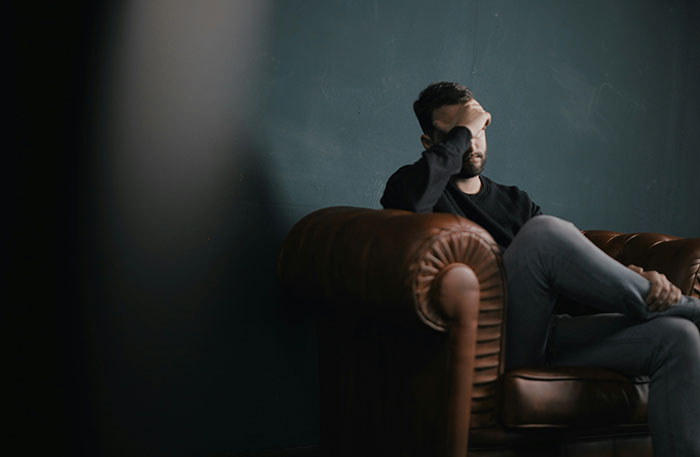 Man looking distressed on a leather sofa, related to expensive long-distance trip challenges. Man looking distressed on a leather sofa, related to expensive long-distance trip challenges.