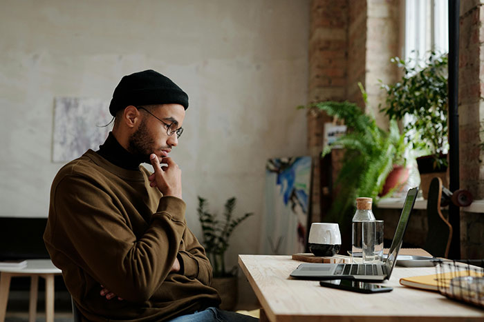 Man in casual attire at a desk, looking at a laptop, contemplating an expensive trip to visit a long-distance girlfriend. Man in casual attire at a desk, looking at a laptop, contemplating an expensive trip to visit a long-distance girlfriend.