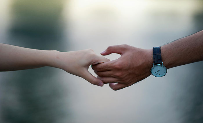 Couple's hands touching softly, man wearing a watch, symbolizing long-distance relationship challenges. Couple's hands touching softly, man wearing a watch, symbolizing long-distance relationship challenges.
