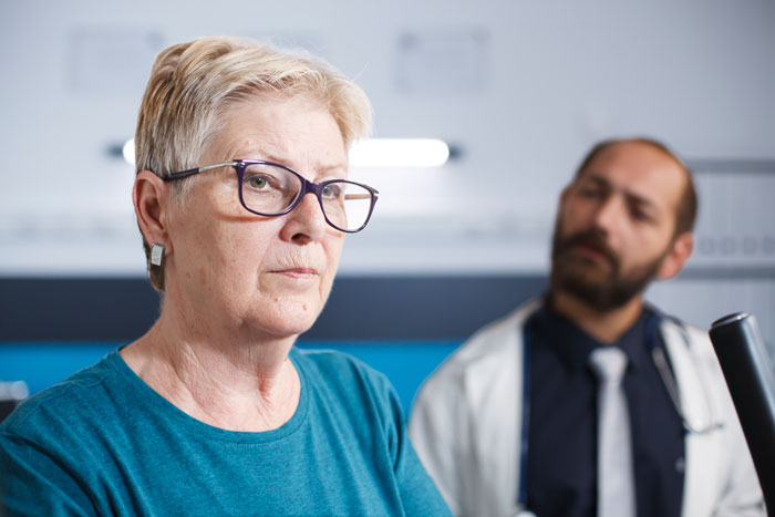 Elderly patient ignored by inattentive doctor, with concerned nurse and upset wife in the background. Elderly patient ignored by inattentive doctor, with concerned nurse and upset wife in the background.