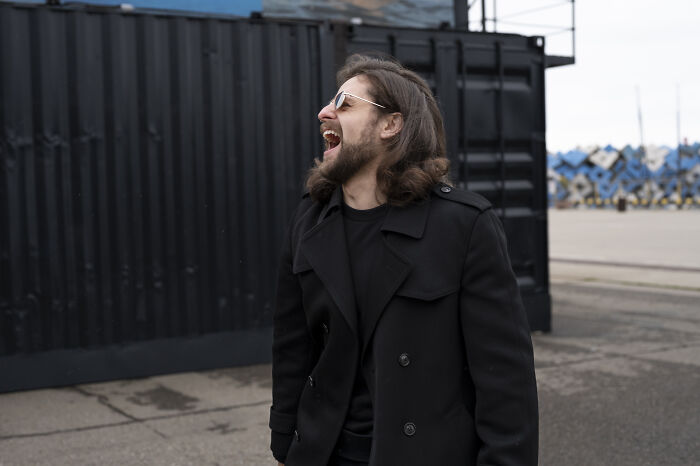 Man wearing sunglasses and black coat laughing outdoors, illustrating usual things changed by the pandemic forever.