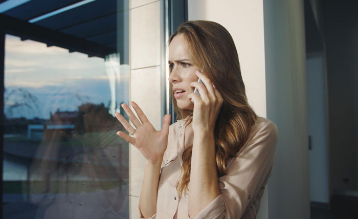Woman looking concerned on a phone call, standing by a window, discussing strangers claiming to be half-siblings. Woman looking concerned on a phone call, standing by a window, discussing strangers claiming to be half-siblings.