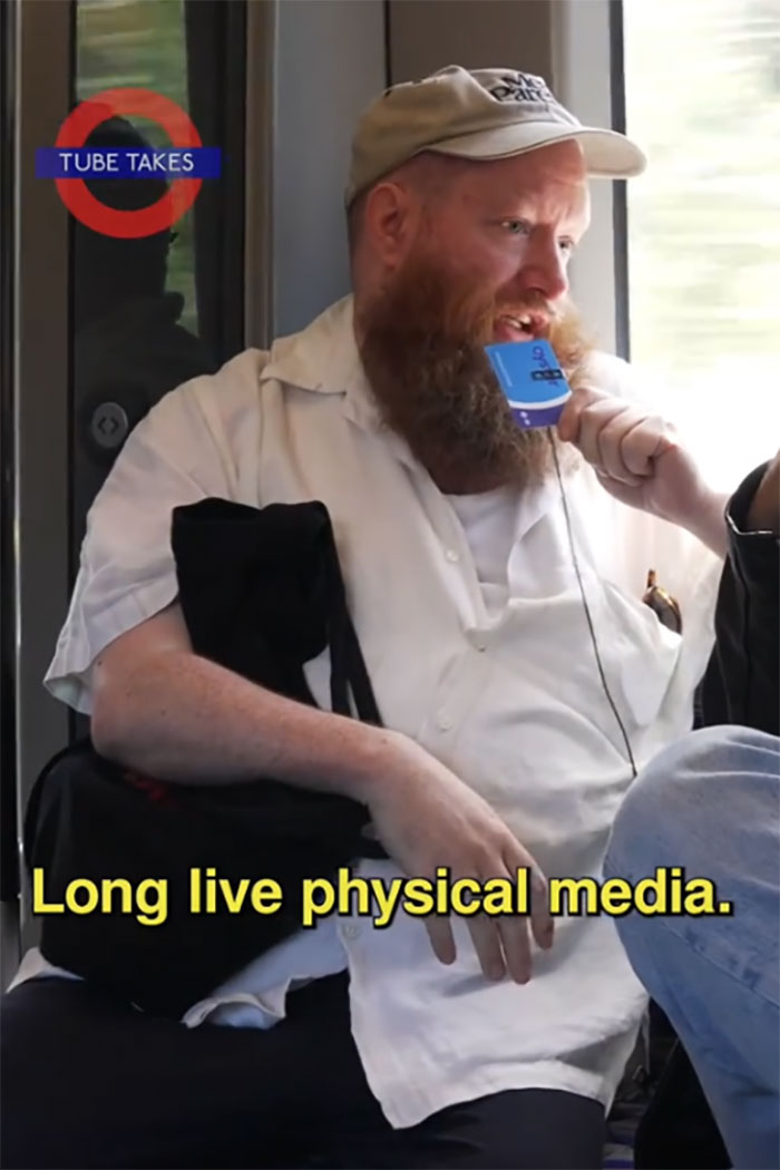 A person on a train discussing physical media, captioned “Long live physical media,” wearing a cap and holding a microphone. A person on a train discussing physical media, captioned “Long live physical media,” wearing a cap and holding a microphone.