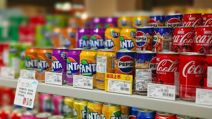 Assorted soda cans on a store shelf, including Fanta, Pepsi, and Coca-Cola, showcasing diverse options.