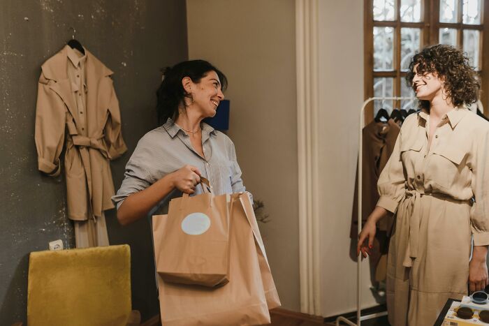 Two women chatting happily in a boutique, with clothes in the background, highlighting adult habits.