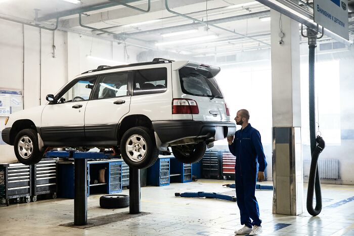 Mechanic inspects car raised on lift in garage, smoke in background.