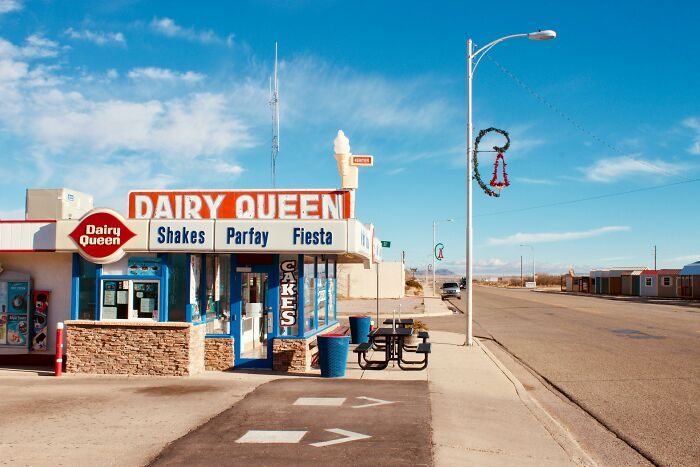 Deserted Dairy Queen on a sunny street, featuring ice cream signage and an empty outdoor seating area.