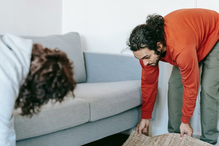 Adults in their 30s moving a rug in living room, highlighting immature habits.