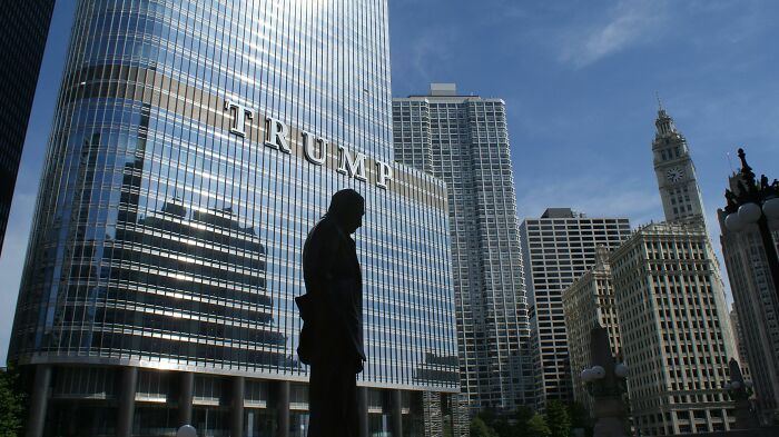 A silhouette of a person in front of a tall glass skyscraper, evoking themes of wealth and luxury.