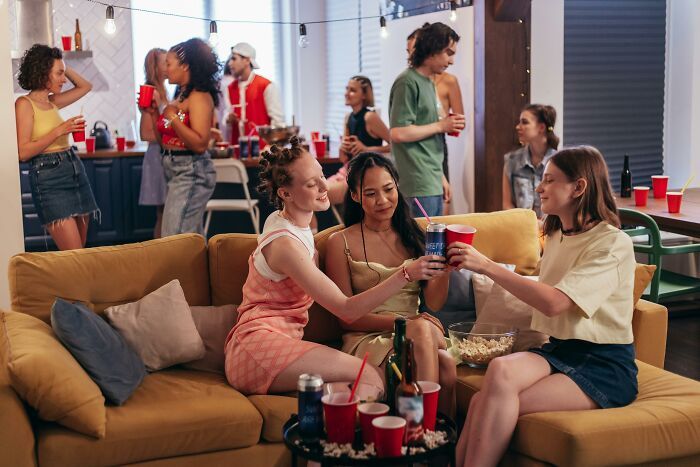Americans at a lively house party with red cups, chatting and enjoying snacks on a cozy couch.