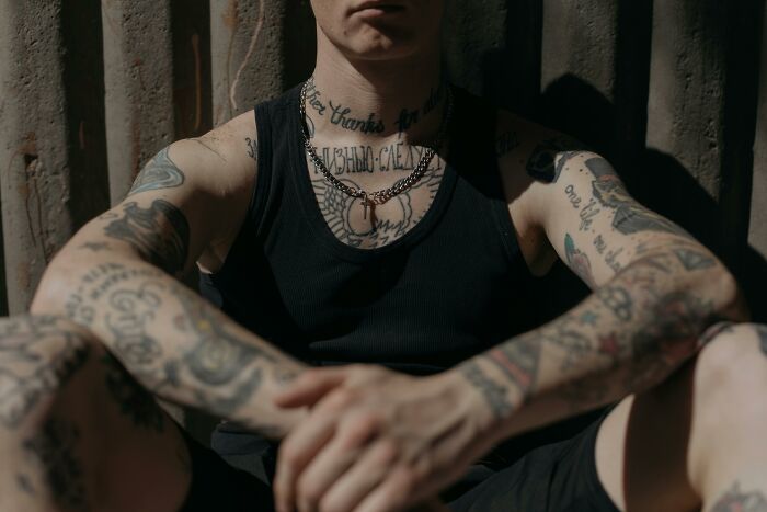 Man with tattoos wearing a black tank top, sitting with arms crossed, showcasing celebrity-inspired ink designs. Man with tattoos wearing a black tank top, sitting with arms crossed, showcasing celebrity-inspired ink designs.