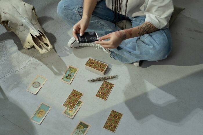 Person sitting on floor with tarot cards and a bundle of sage, exploring archetype discovery and self-reflection. Person sitting on floor with tarot cards and a bundle of sage, exploring archetype discovery and self-reflection.