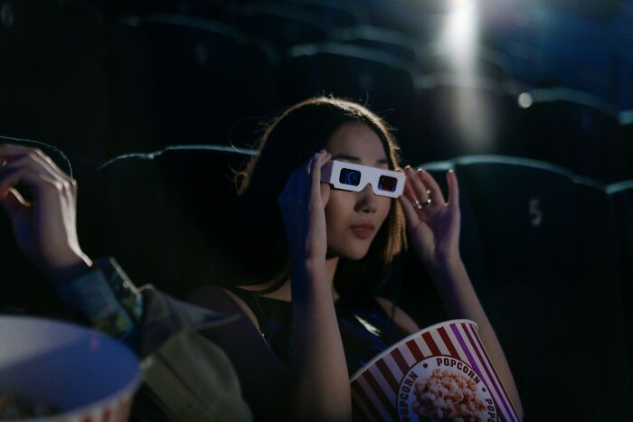 Young woman wearing 3D glasses and holding popcorn while watching a movie in a dark theater for movie title quiz. Young woman wearing 3D glasses and holding popcorn while watching a movie in a dark theater for movie title quiz.