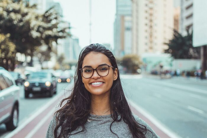 Smiling woman with glasses on a city street, surrounded by everyday things. Smiling woman with glasses on a city street, surrounded by everyday things.