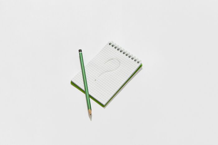 Notepad with question mark sketch and green pencil on white surface, representing plurals challenge and typing test. Notepad with question mark sketch and green pencil on white surface, representing plurals challenge and typing test.