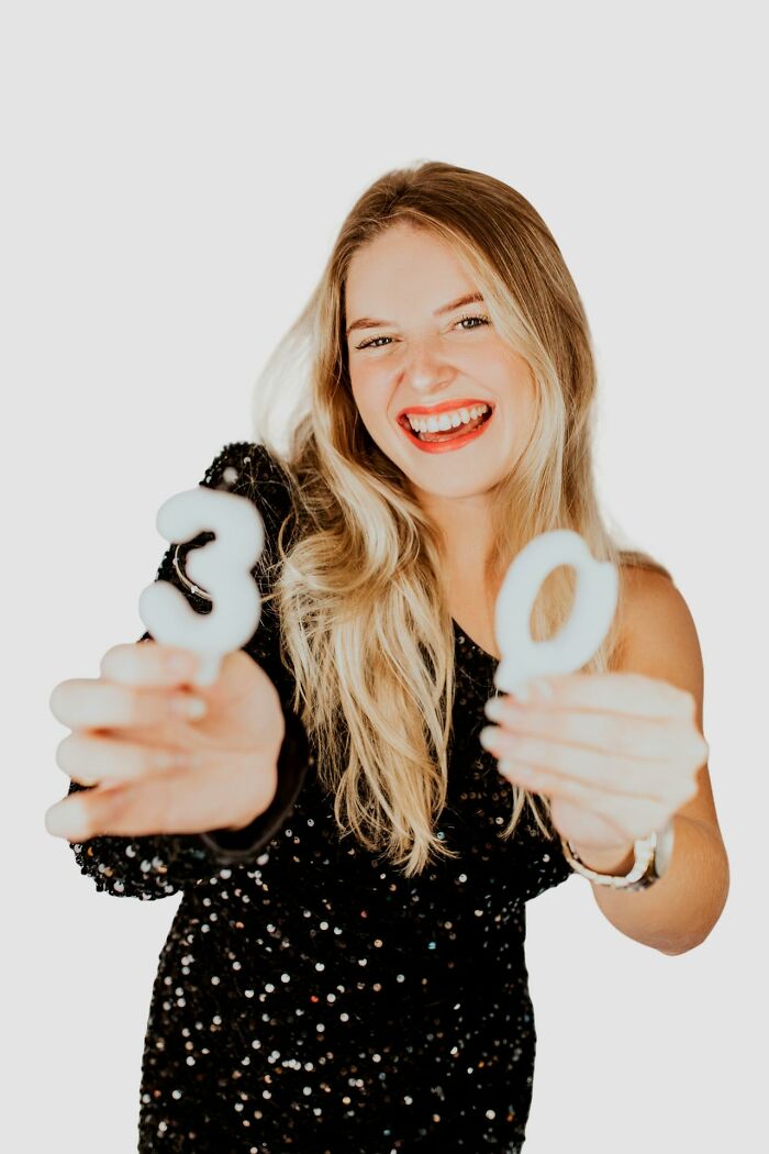 Smiling woman in black dress holding number candles, representing things some women feel embarrassed about.