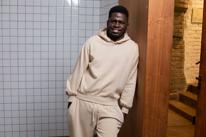 Man in beige hoodie and pants, leaning against a tiled wall, representing American style in casual settings.