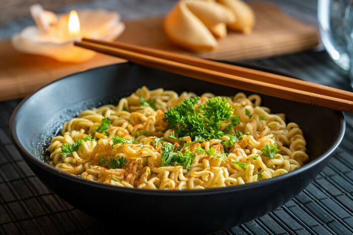 A bowl of noodles with parsley garnish, lit by a candle and accompanied by fortune cookies, represents intrusive thoughts.