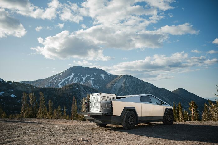 Cybertruck parked with scenic mountain backdrop, showcasing futuristic design under a blue sky.