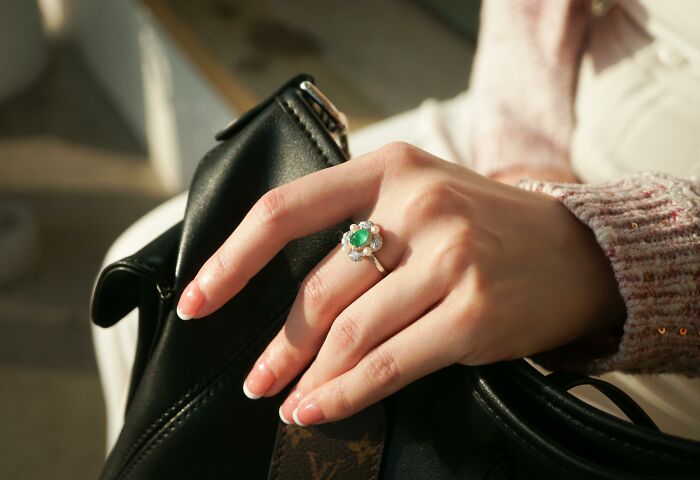 Hand with a large ring on a designer bag, symbolizing pretending to be rich.