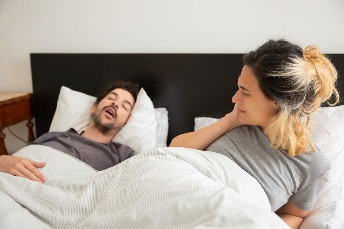 A woman looks amused as a man sleeps, capturing a moment of humor and surprise on April 1st.