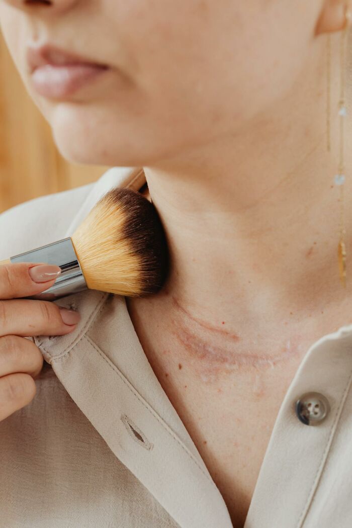 Woman using makeup brush on neck scar, illustrating common female insecurities.