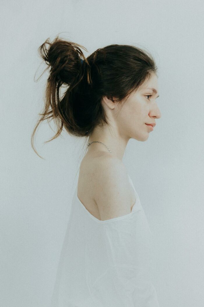 Profile of a woman with messy hair in a white top, showcasing natural beauty often causing embarrassment.