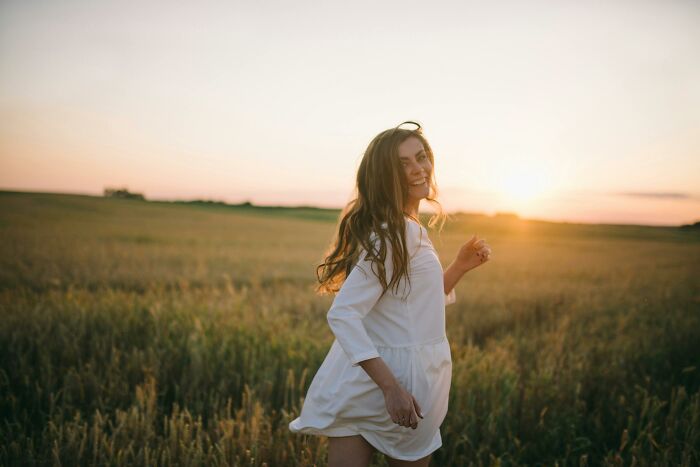 Young woman in a white dress enjoying a sunset in a field, highlighting youthful habits.