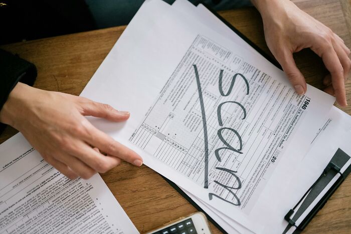 Person holding papers labeled "SCAM" with absolute confidence at a desk.