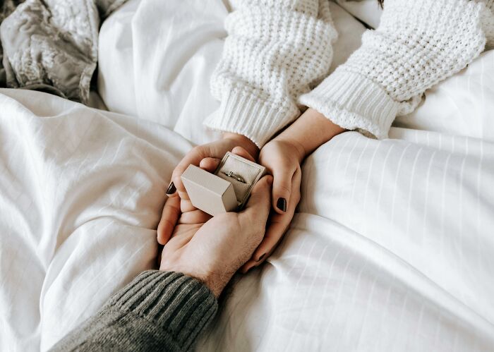 Hands holding an engagement ring box on a bed, highlighting a bridal choice. Hands holding an engagement ring box on a bed, highlighting a bridal choice.