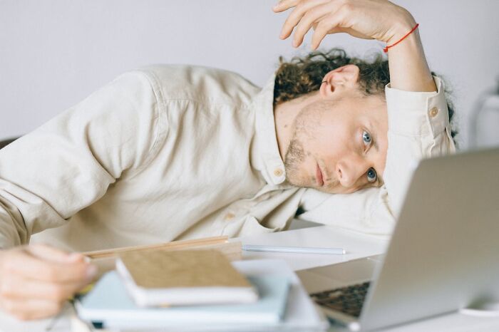 Man with a tired expression, surrounded by notebooks, leaning on desk; possibly feeling fooled on April 1st.