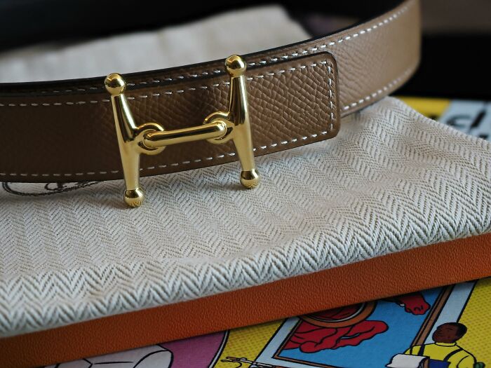 Luxury brown leather belt with gold buckle, placed on designer packaging, symbolizing the illusion of wealth.