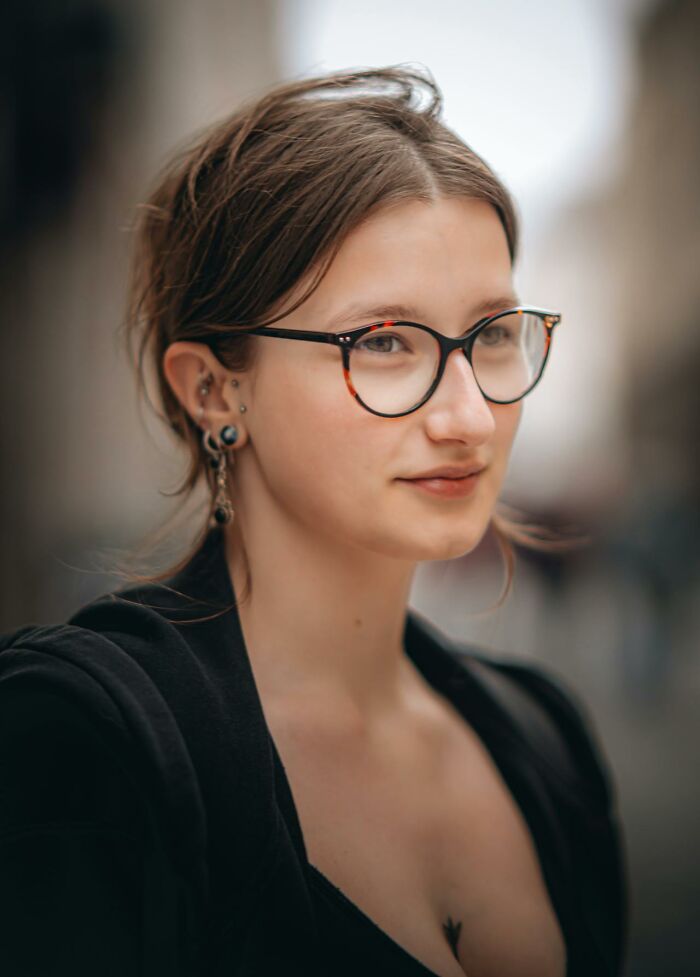Woman with glasses and earrings, looking confident outdoors, reflecting topics that confuse men.