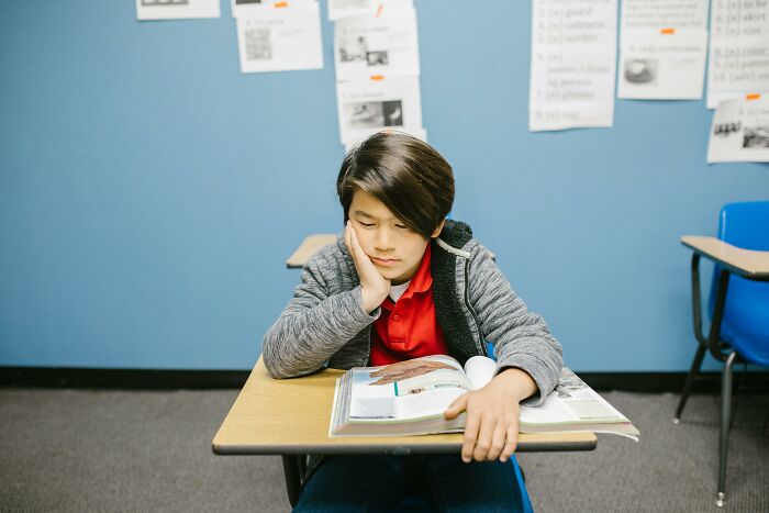 A student sitting at a desk, looking thoughtful with a textbook open, illustrating a moment related to bullying.