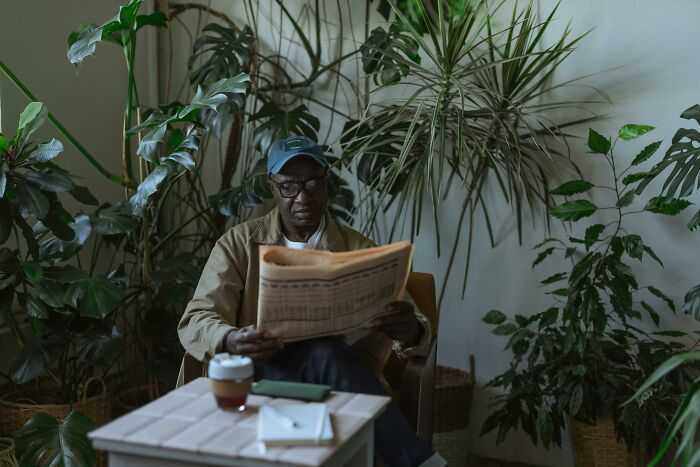 Man reading a newspaper in a cozy plant-filled room, reflecting on intrusive thoughts over coffee.