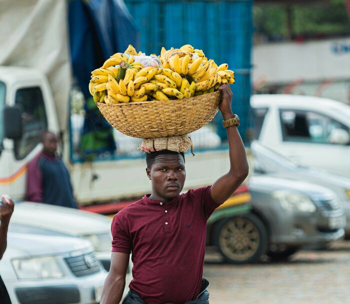 Man carrying basket of bananas on his head, a super normal thing in the country street market scene.